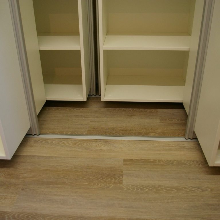 Zwei geöffnete Schranktüren mit leeren Regalen und einem Holzboden darunter.