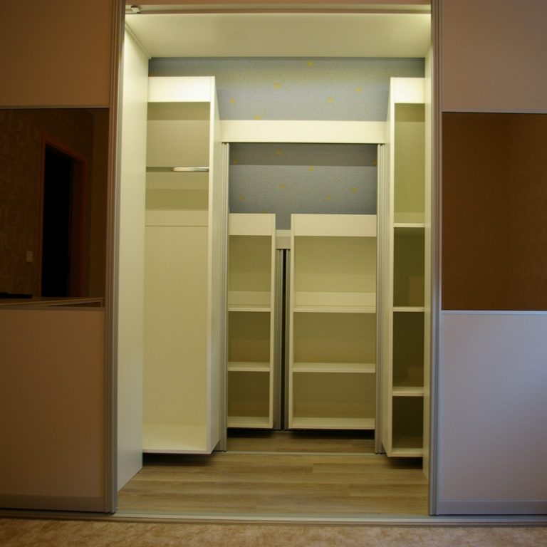 Offener Kleiderschrank mit weißen Regalen zum schieben unter einer Dachschräge nach hinten.